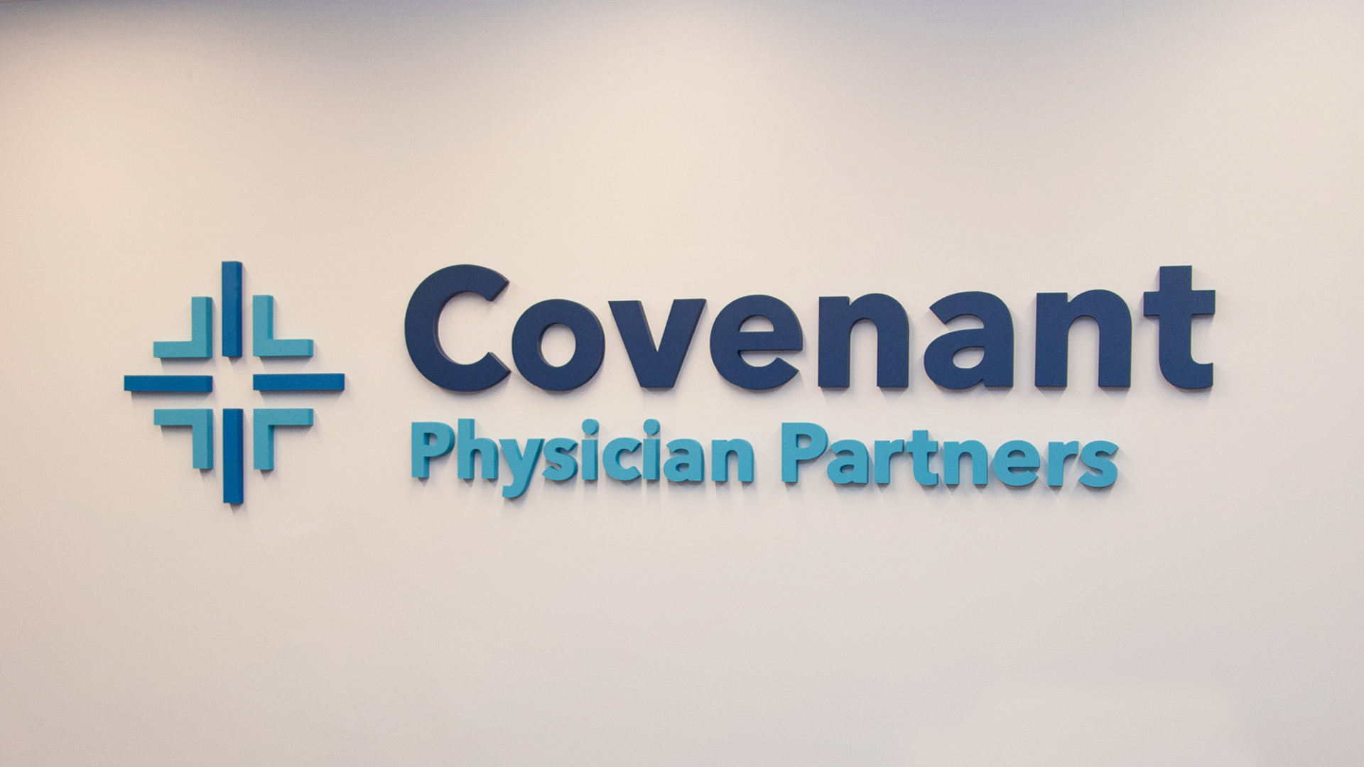Covenant-Image-B An office wall sign with diamond logo and company name that reads "Covenant Physician Partners" in different shades of blue